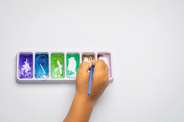 Child's hand dips brush into watercolor palette © Muhammad Azhar