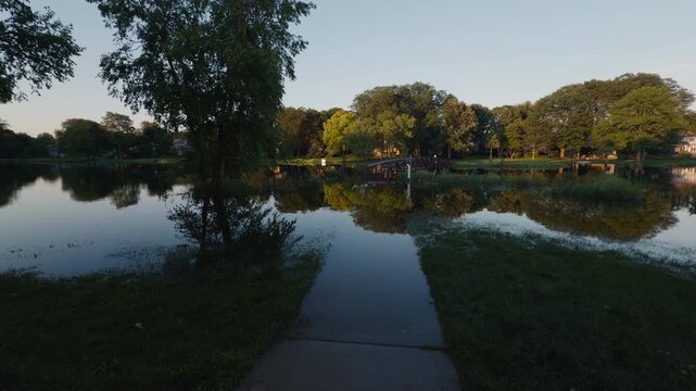 Suburban pond overflowing surrounding grassy shoreline after heavy rainfall, showing localized flooding and high water levels near residential homes.
