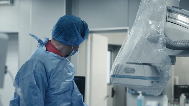 Doctor working beside an angiography system covered with a sterile protective drape during a medical procedure.