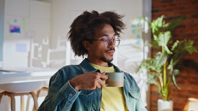 Young designer sipping coffee mug modern loft office. Relaxed work break smile.