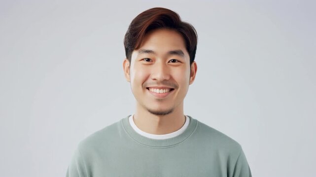 純白の背景で淡い緑のニットを着て控えめに微笑む清潔感のある男性
