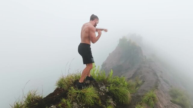 Athletic caucasian man boxing outdoors on a misty mountain peak, demonstrating fitness, strength, and dedication to training in a challenging natural environment. Mount Batur, Bali island, Indonesia