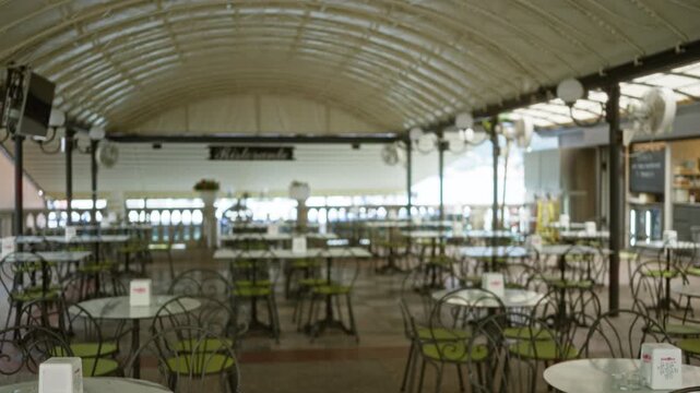 Defocused terrace cafe background with soft bokeh, rows of empty tables and green seat cushions under arched canopy; template overlay virtual.