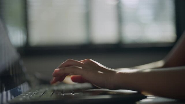 Close-up side view of a hand typing on a computer keyboard in low light, representing data entry, digital technology, office work, information processing, productivity, and online tasks.