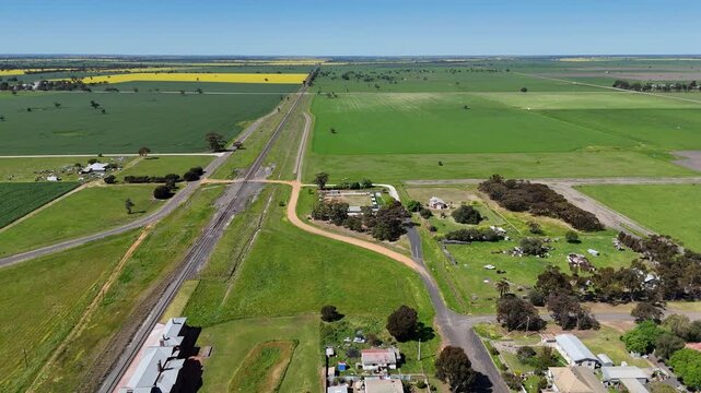 Aerial drone shot of the small border locality of Serviceton, Victoria, Australia, train line passing the historic railway station building,&nbsp;surrounded by vast green pastures and agricultural farmland