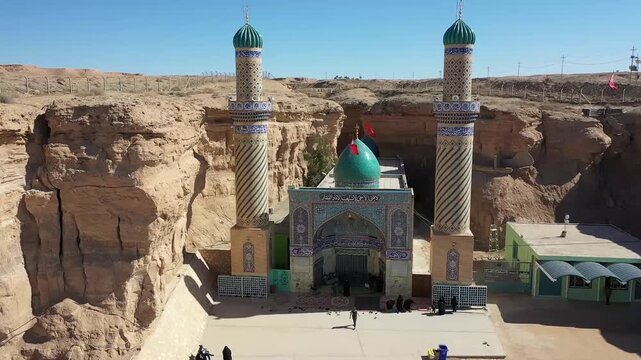 Drone flyover of the Qattarat al-Imam Ali shrine with twin minarets inside a desert canyon, Karbala, Iraq