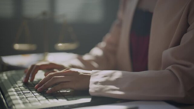 Lawyer working on a computer beside scales of justice in a professional office, representing legal research, case analysis, digital documentation, legislation, and modern law practice.