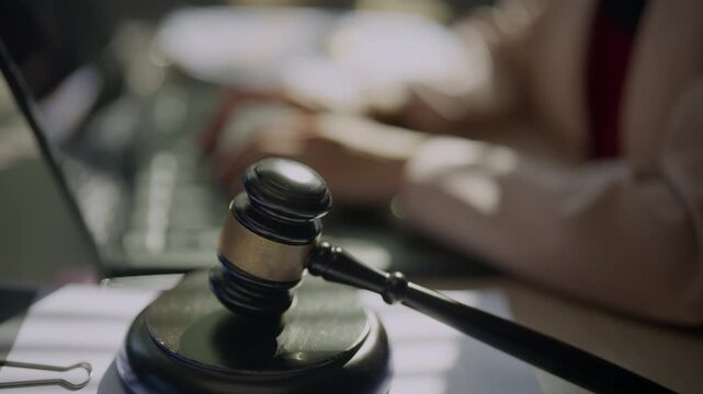 Judge gavel in sharp focus with a legal professional working at a desk in the background, representing law practice, justice, legal consultation, case review, court decisions, and judicial authority.