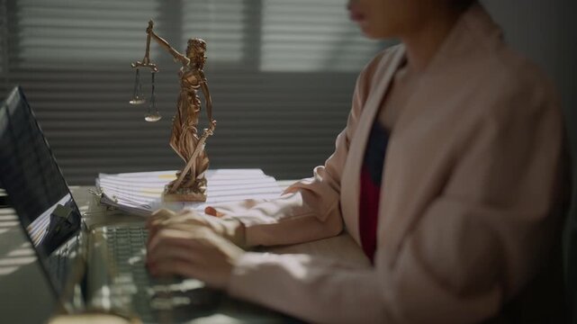 Law office professional typing digital legal documents on a computer with justice scales in the background, representing documentation, compliance, legal administration, technology, and office work.