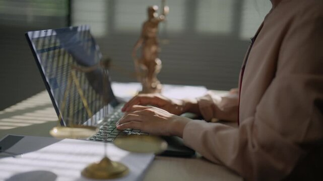 Legal professional typing on a computer with Lady Justice statue in the background, representing legal research, digital documentation, case preparation, law practice, and modern legal services.