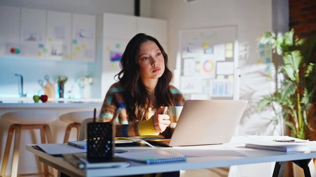 Designer thinking with coffee cup laptop. Camera pulls back bright home office.