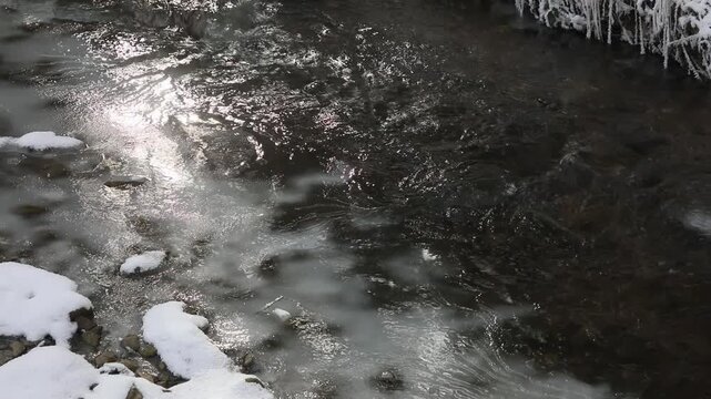 Water flowing over an ice surface with light reflections on the water surface, Mondseeland, Salzkammergut, Austria