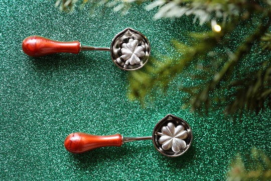 Clover Leaf Sealing Spoons on Green Background.metal casting set on green glitter for tin pouring instructions,holiday gift sets,good luck and traditional European holiday rituals.