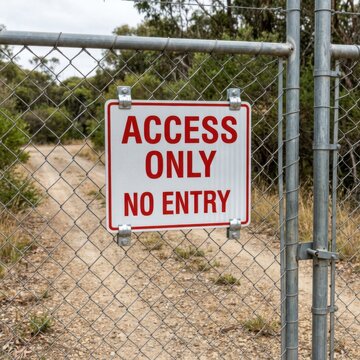 Restricted Area Access Only No Entry Sign on Chain Link Fence at Dirt Road Entrance