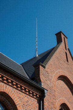 Metal lightning rod installed on red brick roof of historic old building. Architectural detail of lightning protection system against clear blue sky. Traditional European architecture with weather