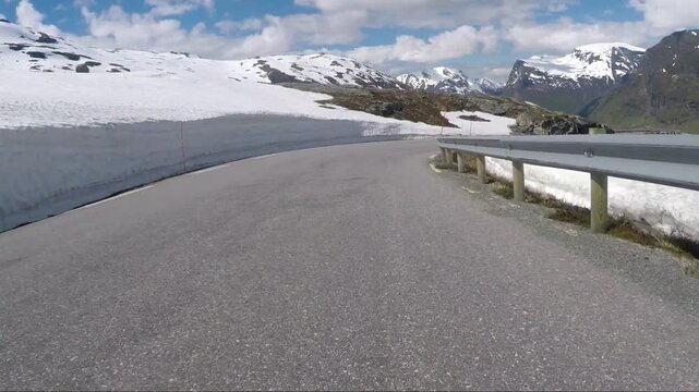 Snow-covered mountains flank a winding mountain road on a clear day, May, spring in the mountains of Norway, driving down to Geiranger, Norway