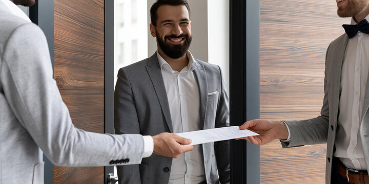 Two men in suits are exchanging a document. A third man smiles in the background.