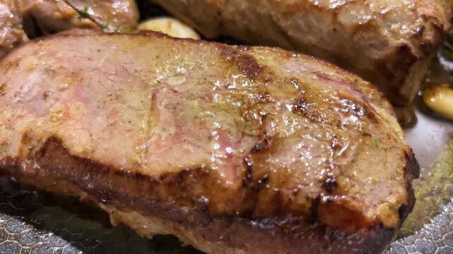 Cooked veal medallions sit seared in a hot pan after frying, showcasing thick tenderloin steaks infused with fresh rosemary, whole garlic cloves, and aromatic thyme.