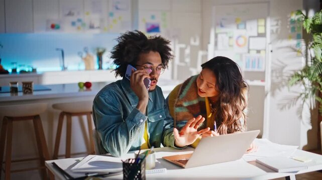 Business partners talking phone home office. Woman pointing laptop screen notes.