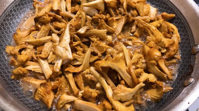 Chanterelle mushrooms frying in a modern honeycomb pan as golden wild fungi simmer close-up with boiling liquid and sliced fresh elements cooking in a culinary recipe.