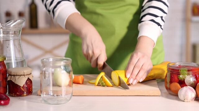 Making pickles. Woman cutting zucchini and putting it into glass jar at white wooden table indoors, closeup