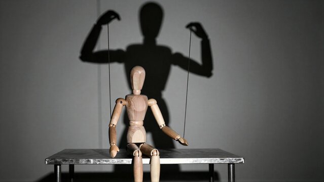 Wooden puppet sits on table, shadowed by a.