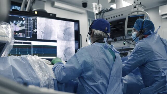 Interventional specialists monitoring vascular imaging and hemodynamics in a hospital cath lab.