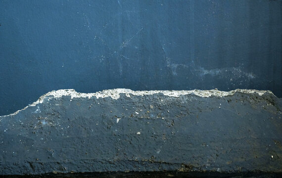 Abstract shot of a dark blue textured wall with a damaged rough concrete ledge, creating a minimalist architectural background. Textured background