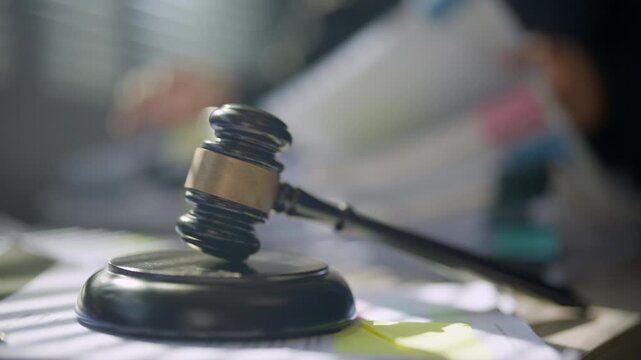 Court gavel placed on a professional office desk with a person working in the background, representing justice, legal decisions, litigation, judicial proceedings, authority, and law services.