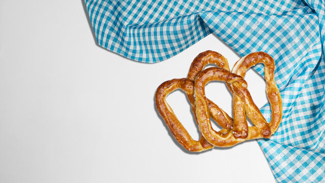 Freshly baked pretzels arranged neatly with a blue and white checkered napkin on a clean white background, viewed from above. Bavarian Oktoberfest Festival