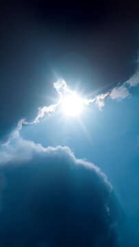 Bright sun shining through dark, dramatic clouds in a clear blue sky, creating a stunning contrast of light and shadow, with sun rays radiating outward. Nature, natural, or quotes background