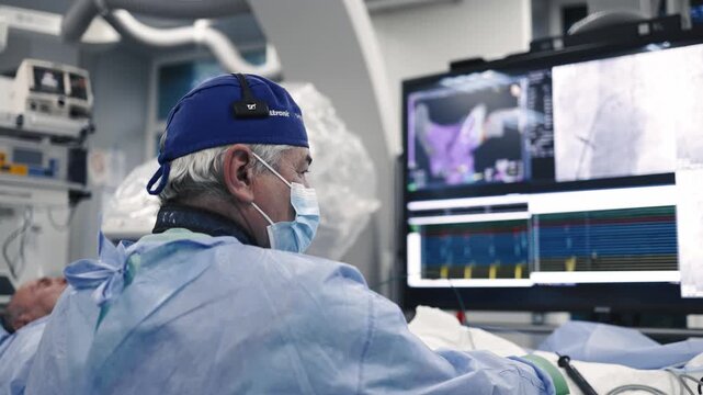 Cardiologist monitoring vascular imaging and medical data on a large screen in a hospital cath lab.