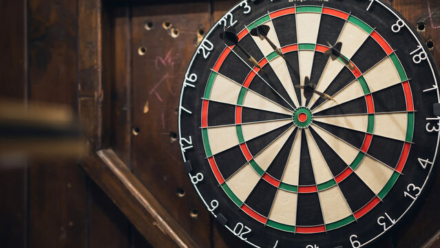 Close-up dartboard with darts mid-throw in dimly lit bar setting