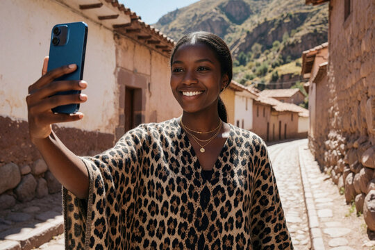 Smiling Latina woman takes selfie with smartphone in Bolivian village. Beautiful dark skinned female tourist wears leopard print poncho walking on narrow street. Happy girl enjoys travel journey,
