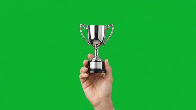 Hand holding a shiny metallic winner trophy cup isolated against a vibrant green screen background for professional achievement and success display