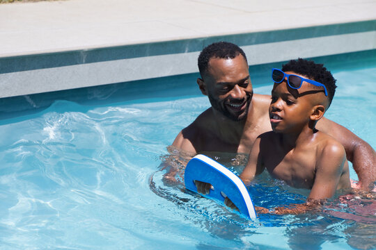 African American shirtless father with teen son playing at pool with blue swimming board and shades