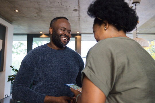 African American couple laughing and sharing smartphone at home wearing navy sweater and olive tee
