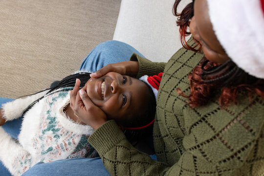 African mother and child cuddling on light-colored couch in living room with green knitted sweater