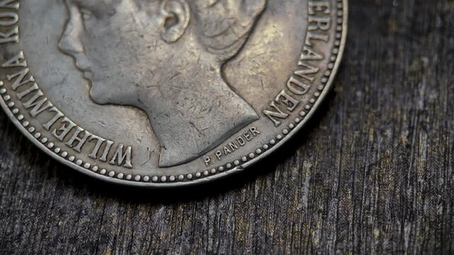 Macro detail video of an antique Dutch gulden crown coin focusing on the small engraver signature mark beneath the portrait neck,and distinctive historical numismatic details.