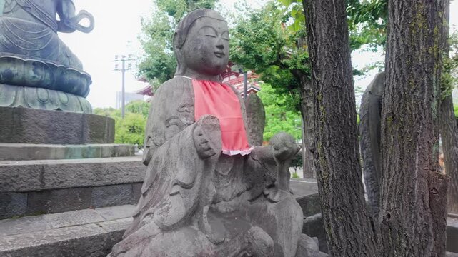 A stone Jizo statue wearing a red bib sits on the historic temple grounds of Sensō-ji in Asakusa, Taito City, Tokyo, Japan.