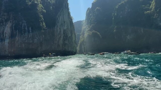 Boat wake foaming on turquoise water while leaving a lagoon framed by tall limestone cliffs in Phi Phi Krabi Thailand