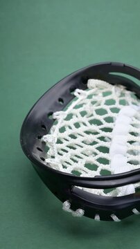 pan view yellow lacrosse ball rests on the head of a black lacrosse stick with white netting at vertical composition