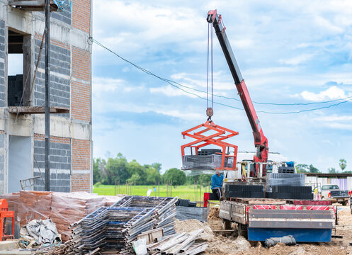 A mobile crane mounted on a flatbed truck lifting concrete masonry blocks using a specialized scissor grab attachment at a building construction site.