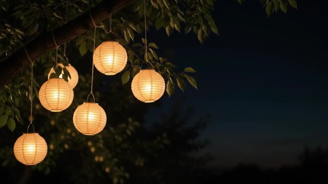 Warm glowing paper lanterns hanging on tree branches at night with dark copy space for outdoor garden party