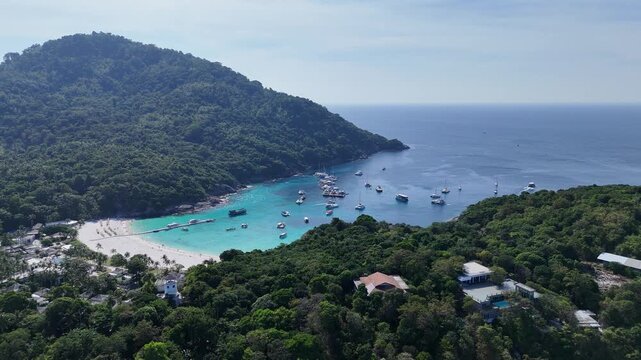 Aerial view of a sheltered bay with many anchored boats below forested hills on a tropical island in Racha Island Phuket Thailand