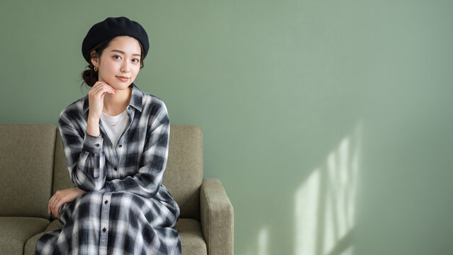ベレー帽とチェック柄シャツを着てソファに座る女性