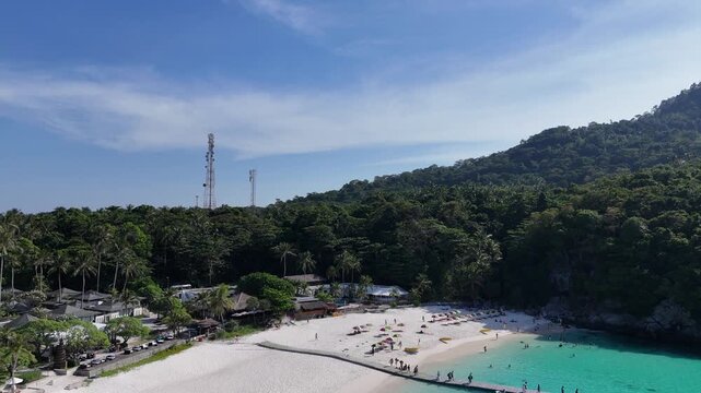Aerial view of a white sand beach with a long pier and resort below a jungle covered hill in Racha Island Phuket Thailand