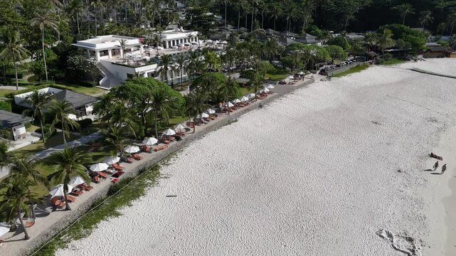 Aerial flight over anchored boats in a turquoise bay to a white sand beach and resort villas in Racha Island Phuket Thailand