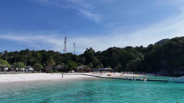 Low aerial flight over clear turquoise water toward a white beach pier and speedboats in Racha Island Phuket Thailand