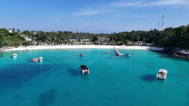 Aerial view of speedboats in a bright turquoise bay with a white sand beach and palm trees in Racha Island Phuket Thailand